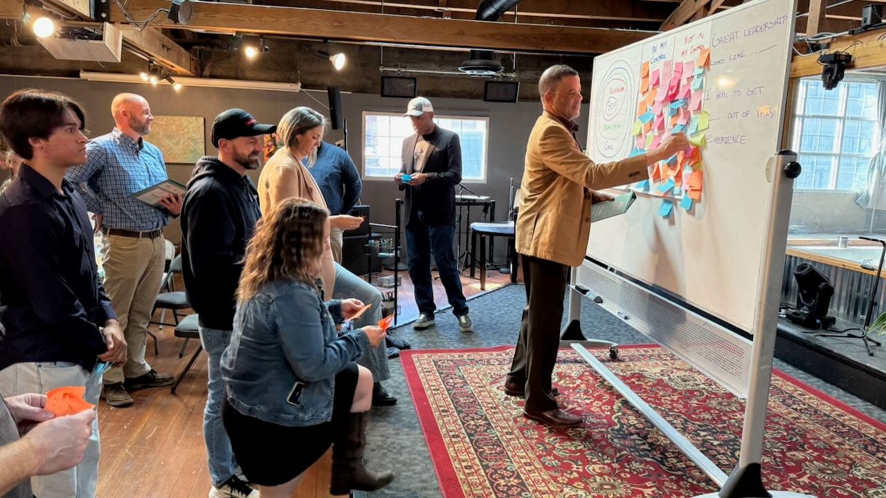 Leadership cohort participants gathered around a whiteboard with sticky notes at The Hivve